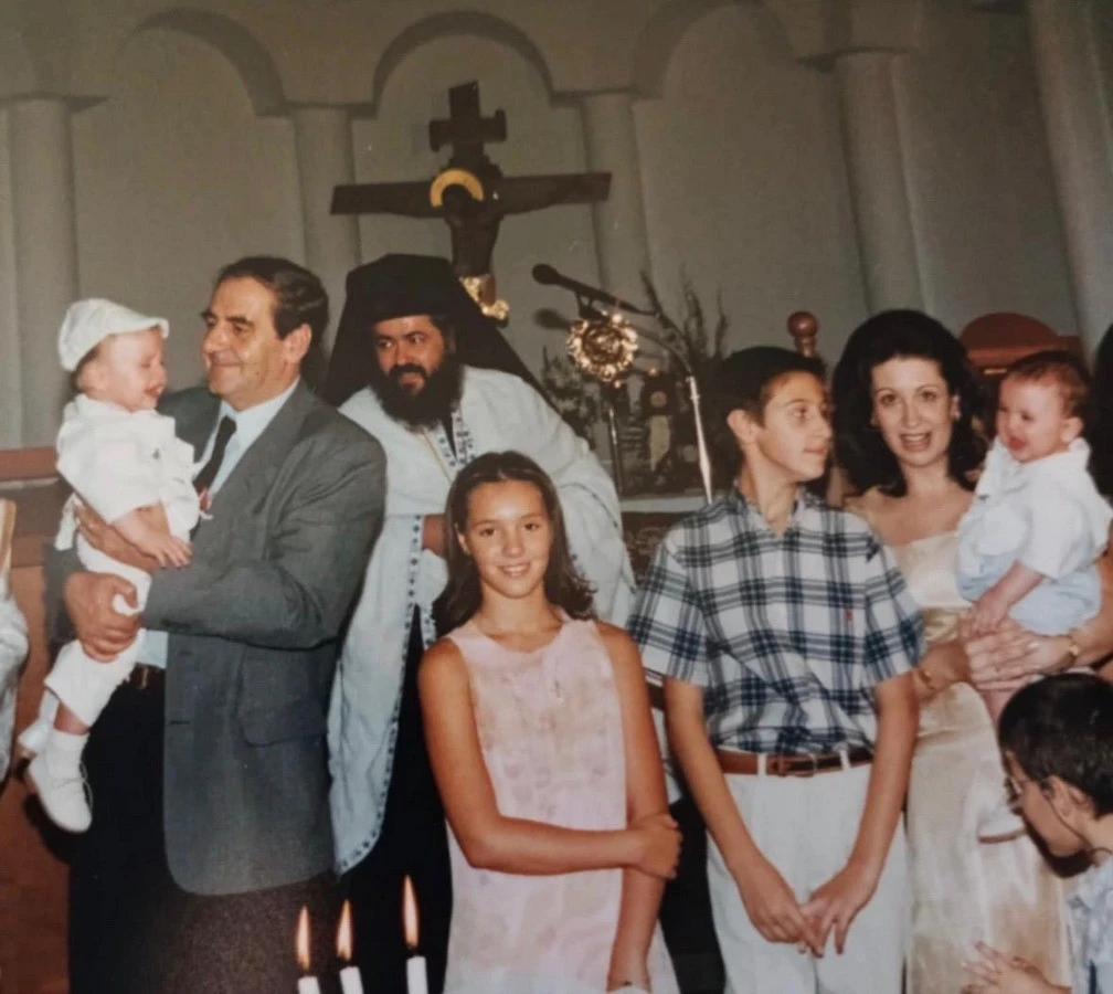 Οικογενειακή φωτογραφία από τη βάφτιση των δίδυμων αδελφών του. Διακρίνονται ο πατέρας του Κώστας, η μητέρα του Βάσω, ο ίδιος στη μέση, η νονά και πίσω ο σημερινός Μητροπολίτης Σταυρουπόλεως και Νεαπόλεως Βαρνάβας.